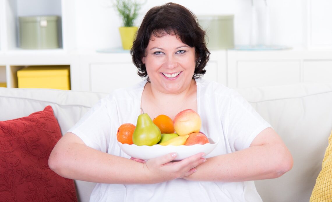 Eine Frau sitzt auf einem Sofa, freut sich über eine Schüssel voll Obst