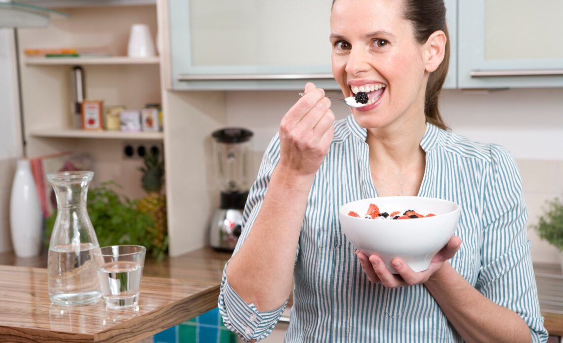 Eine Frau isst Joghurt mit Früchten.